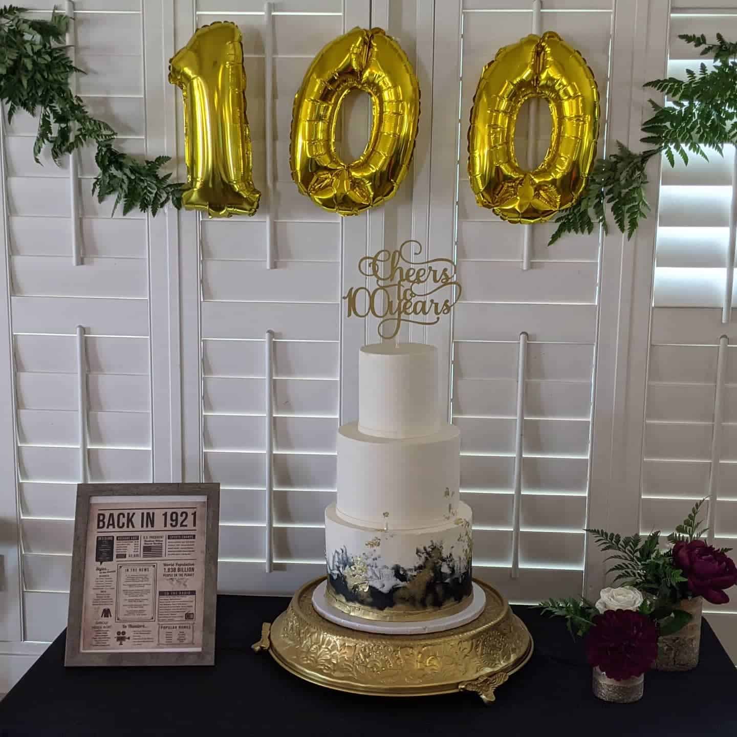10th anniversary cake with gold "100" balloons and floral decorations.