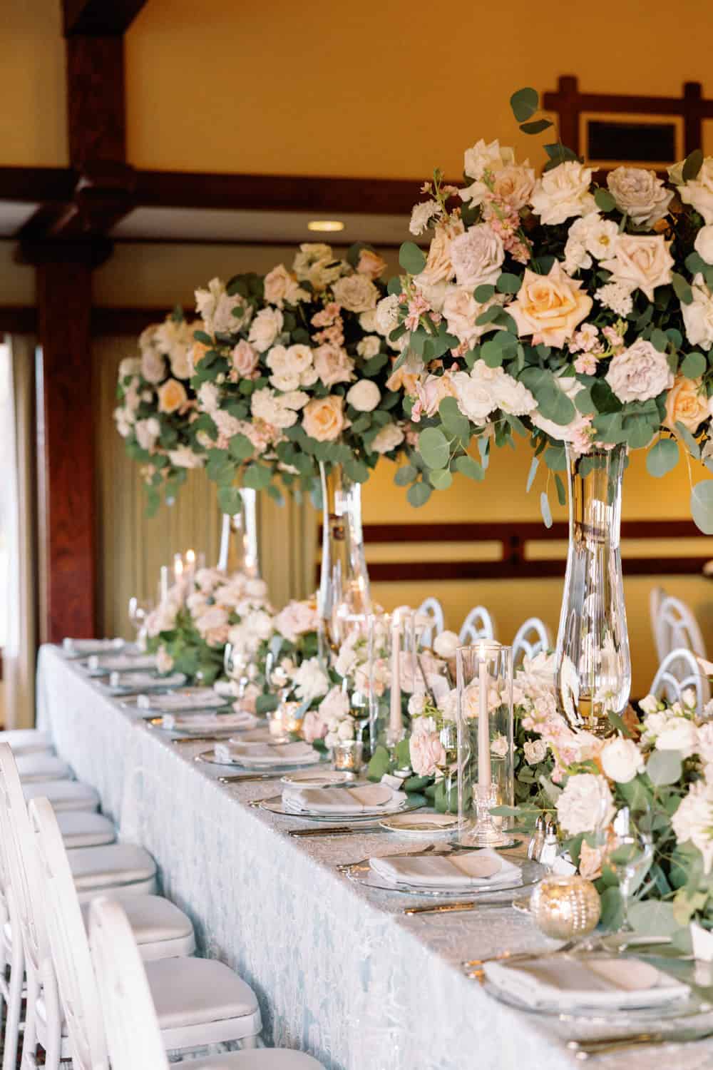 Elegant floral wedding table centerpiece with tall vases filled with roses and greenery.