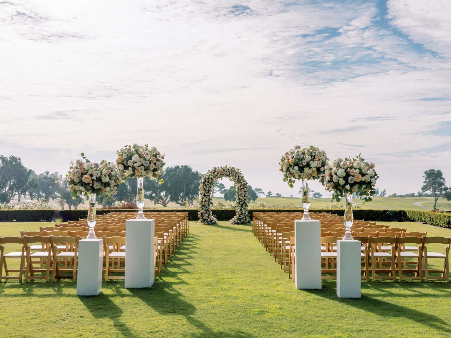 Elegant outdoor wedding ceremony with floral arch and wooden chairs on lush green grass.