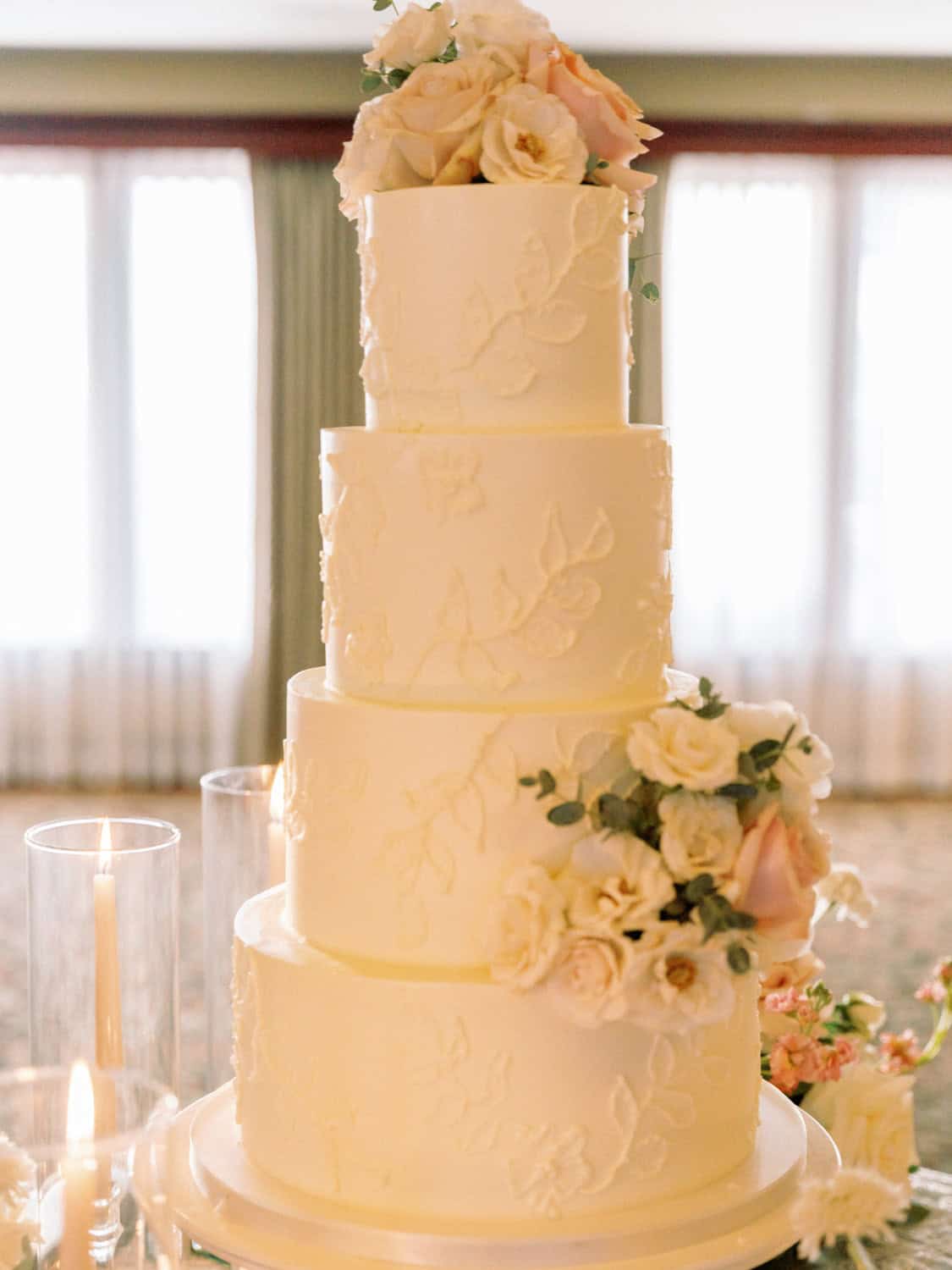 Wedding cake with white roses and blush peonies, four-tiered with delicate floral decorations.