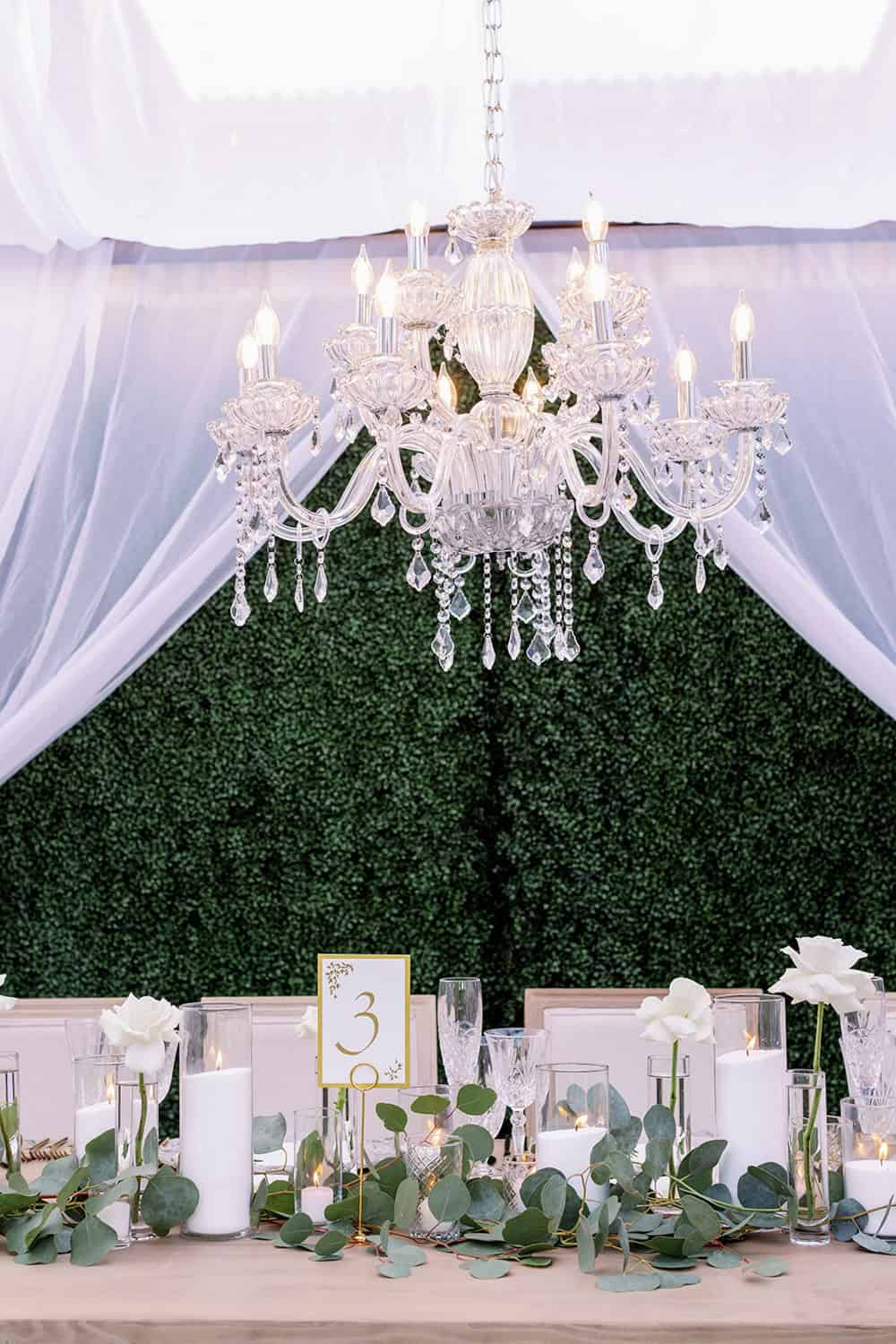 Elegant crystal chandelier above a beautifully decorated event table with greenery and candles.