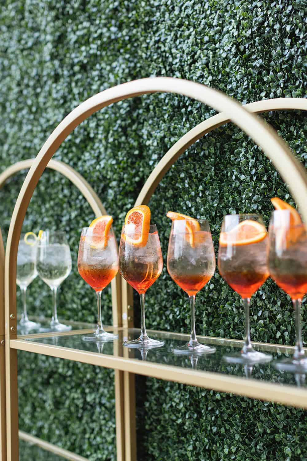Elegant cocktails with orange slices on a gold bar cart at a stylish event.