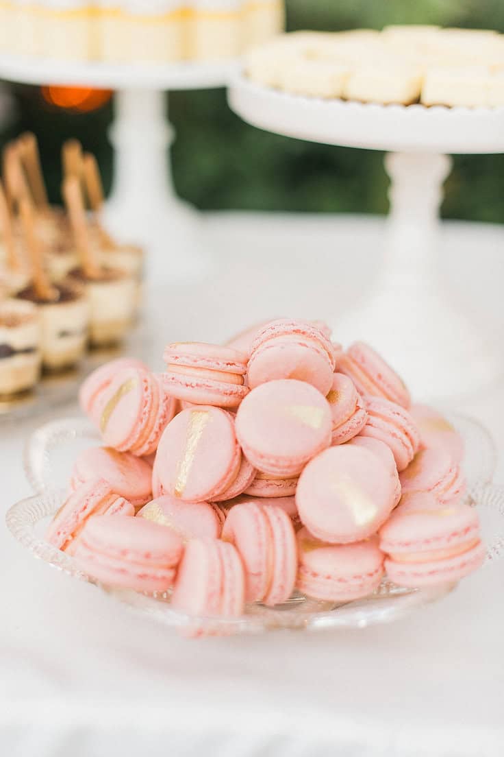 Delicious pink macarons arranged on a glass plate for a dessert table at a soirée.