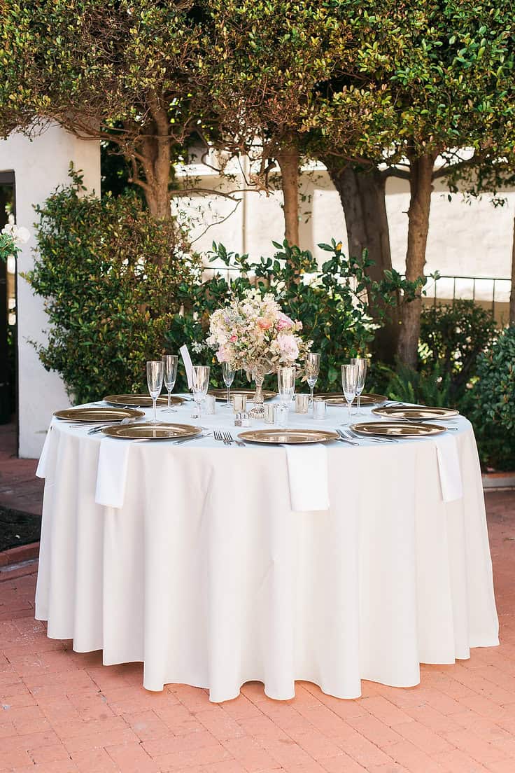 Outdoor dining table with white tablecloth, floral centerpiece, and glassware.