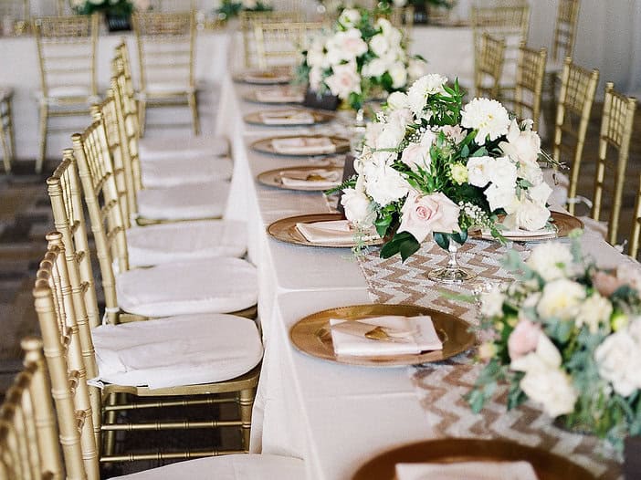 Wedding reception table decorated with white flowers and gold chairs for elegant event.
