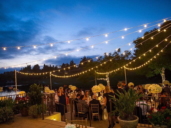 Outdoor evening event with string lights, floral arrangements, and guests enjoying a sophisticated g.