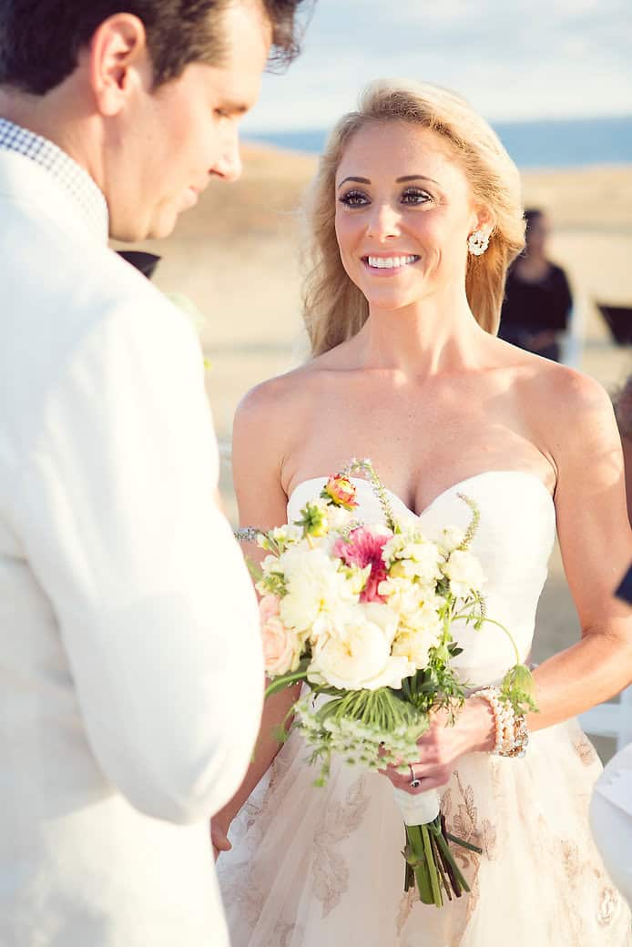 Bride holding a beautiful bouquet, smiling at groom during outdoor wedding ceremony.